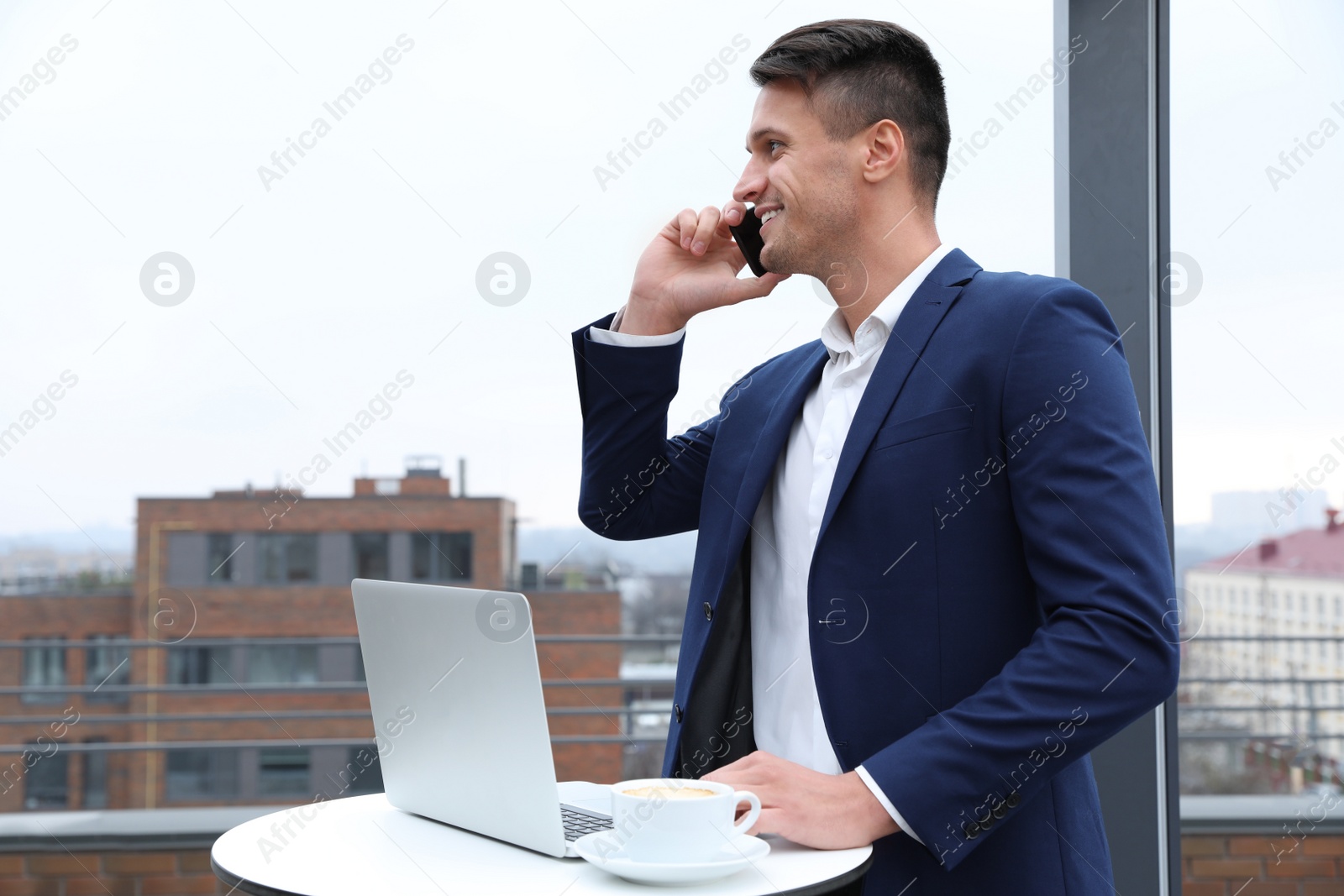 Photo of Businessman with laptop talking on phone in outdoor cafe. Corporate blog