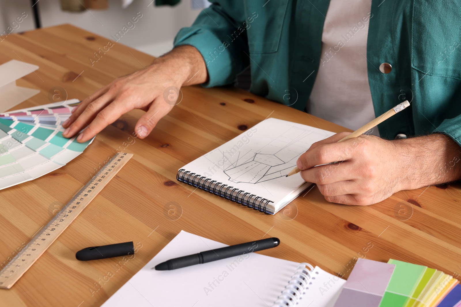 Photo of Man drawing in sketchbook with pencil at wooden table, closeup