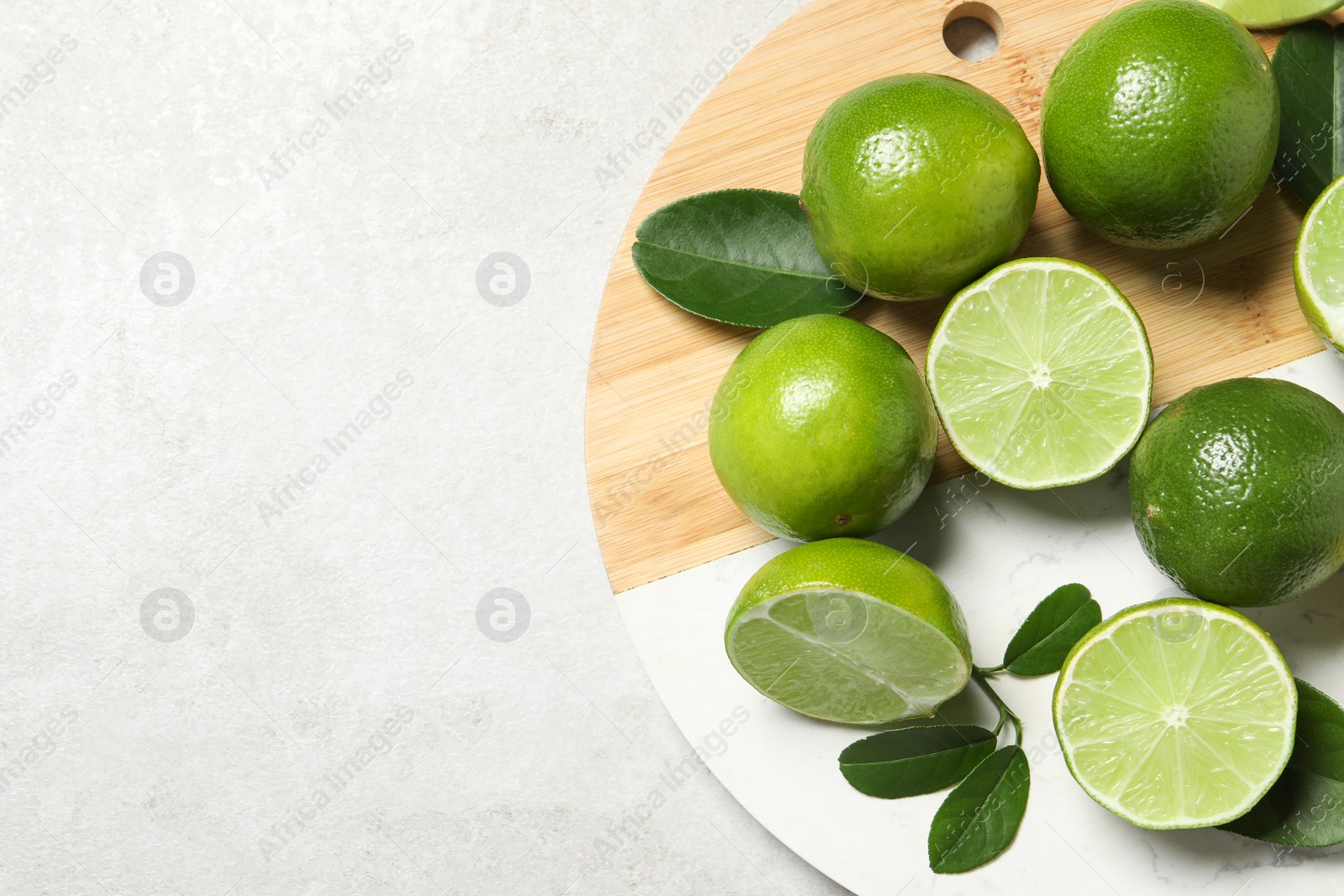 Photo of Fresh ripe limes and leaves on light table, top view. Space for text