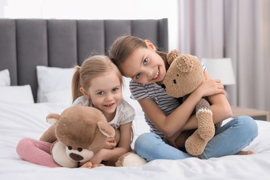 Photo of Cute little sisters with teddy bears on bed at home