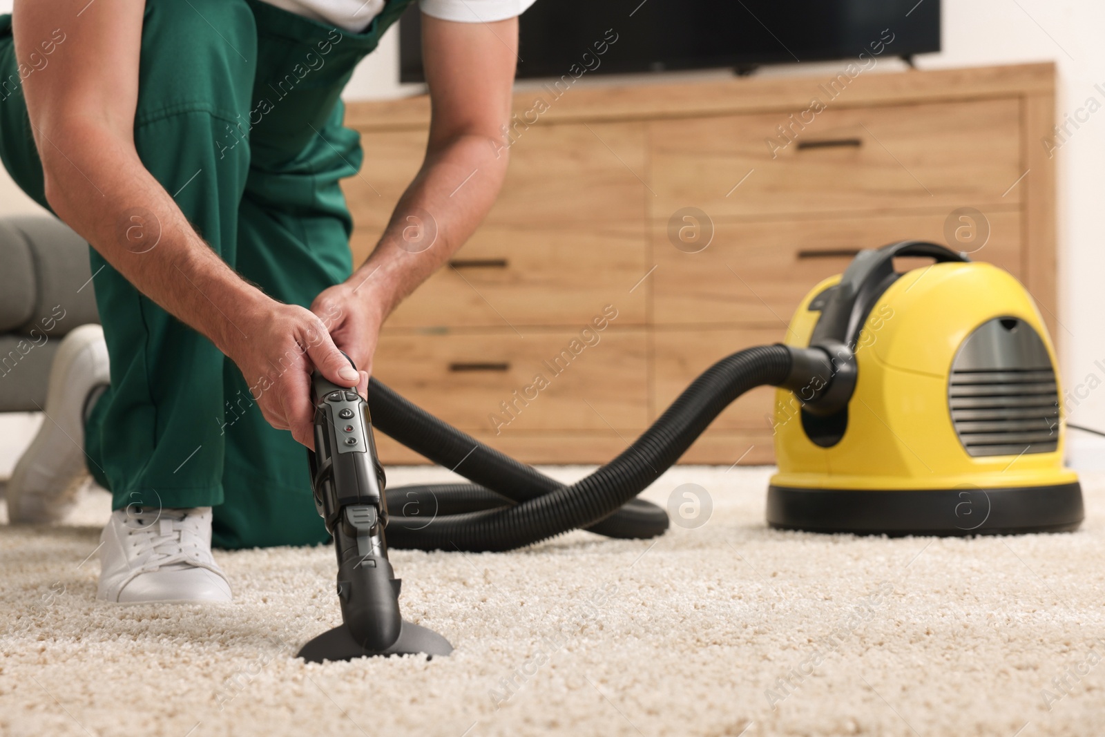 Photo of Dry cleaner's employee hoovering carpet with vacuum cleaner indoors, closeup