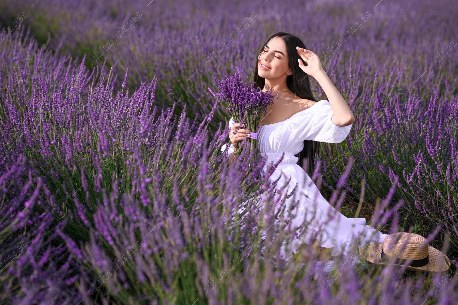 Photo of Beautiful young woman with bouquet sitting in lavender field