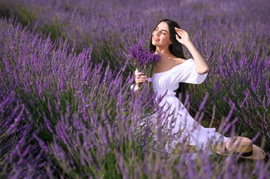 Beautiful young woman with bouquet sitting in lavender field