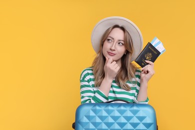 Photo of Young woman with passport, ticket and suitcase on yellow background, space for text