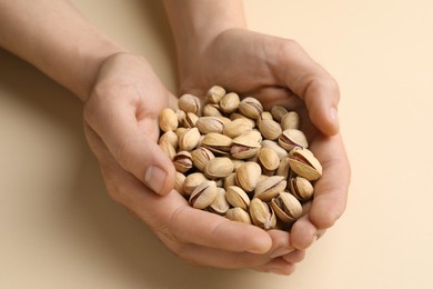 Woman holding tasty roasted pistachio nuts on beige background, closeup