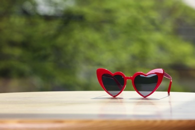 Photo of Stylish heart shaped sunglasses on table against blurred background. Space for text