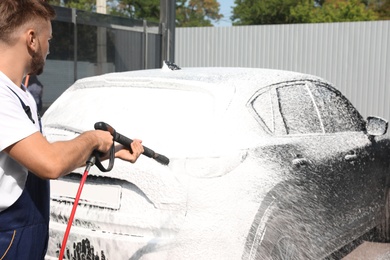 Young worker cleaning automobile with high pressure water jet at car wash