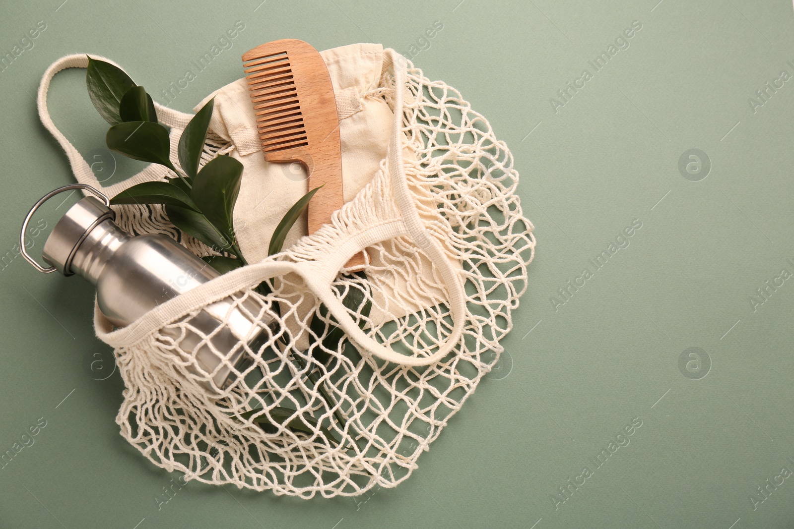 Photo of Fishnet bag with different items on pale green background, top view and space for text. Conscious consumption