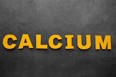 Photo of Word Calcium made of orange paper letters on black background, top view