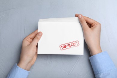 Image of Top Secret stamp. Woman with envelope at grey table, top view