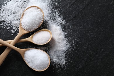 Organic salt in spoons on black table, flat lay. Space for text