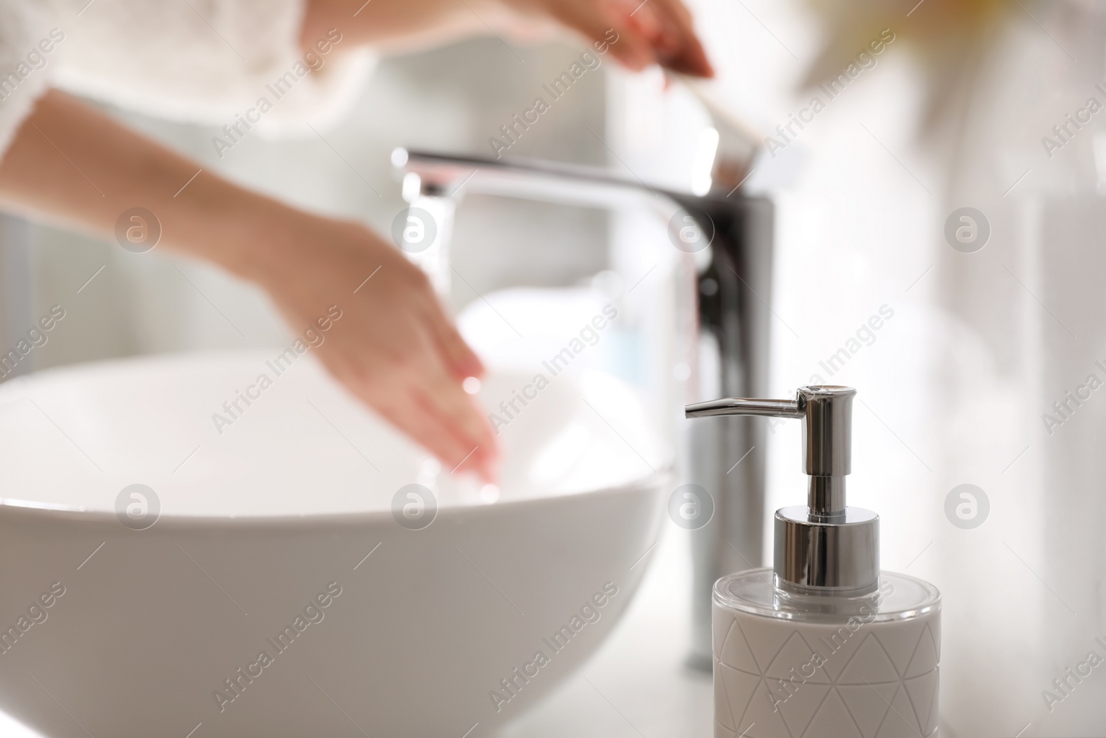 Photo of Woman washing hands over sink in bathroom, focus on soap dispenser