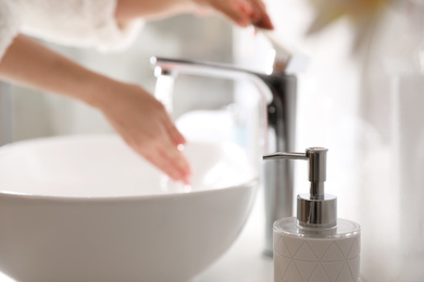 Woman washing hands over sink in bathroom, focus on soap dispenser
