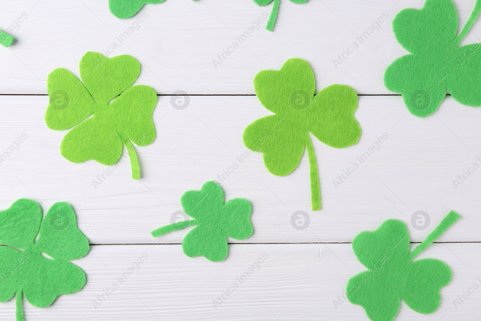 Photo of St. Patrick's day. Decorative green clover leaves on white wooden table, flat lay