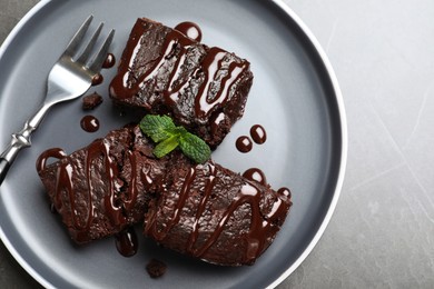 Delicious chocolate brownies with sweet syrup and mint served on grey table, top view