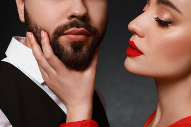 Woman touching bearded man's face on dark background, closeup