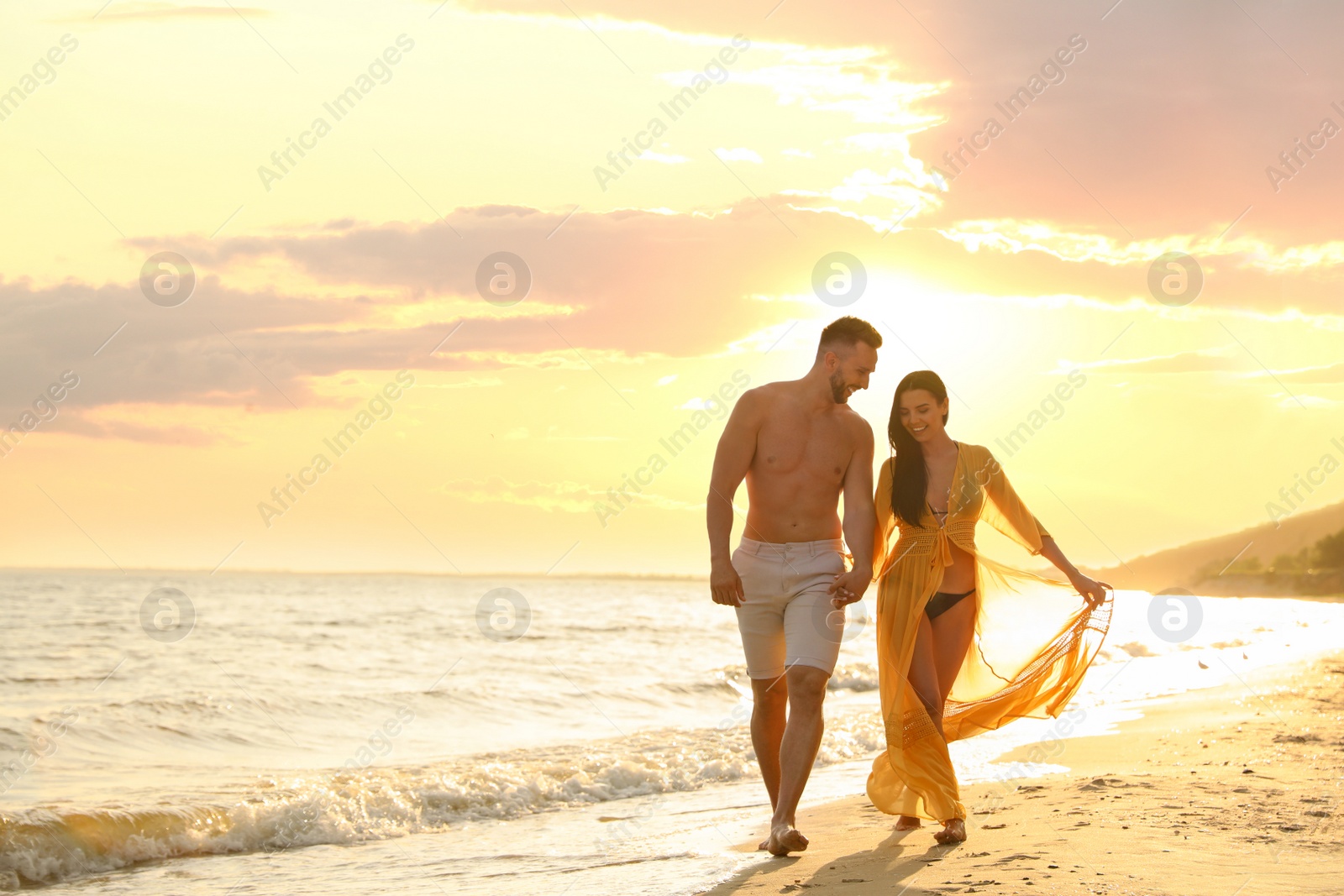 Photo of Happy young couple walking together on beach at sunset