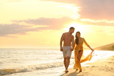 Photo of Happy young couple walking together on beach at sunset