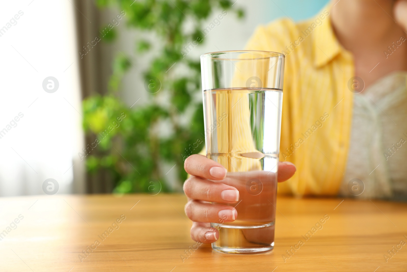 Photo of Woman holding glass of water at wooden table, closeup with space for text. Refreshing drink