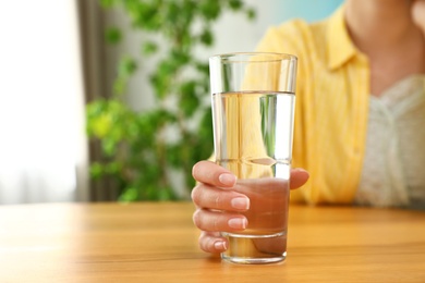 Woman holding glass of water at wooden table, closeup with space for text. Refreshing drink
