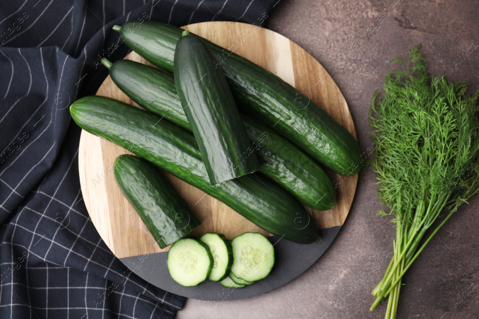 Photo of Fresh cucumbers and dill on brown textured table, top view