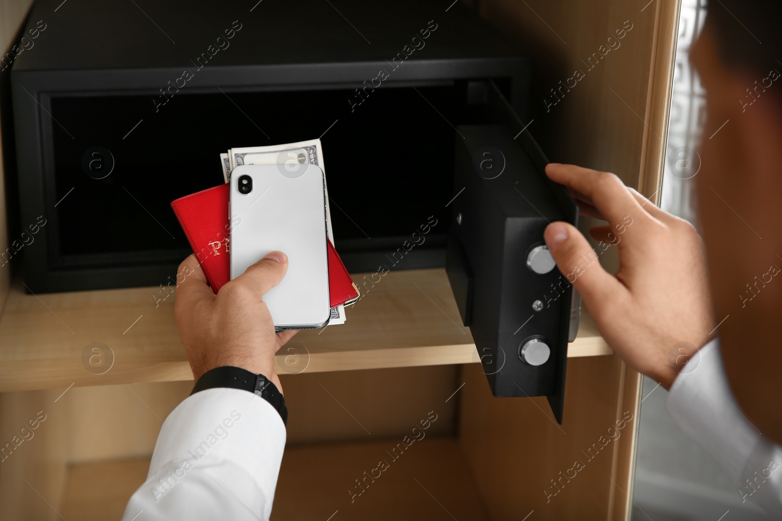 Photo of Man putting smartphone, passport and money into steel safe, closeup