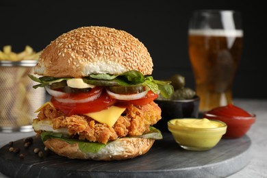 Photo of Delicious burger with crispy chicken patty and sauces on grey table, closeup