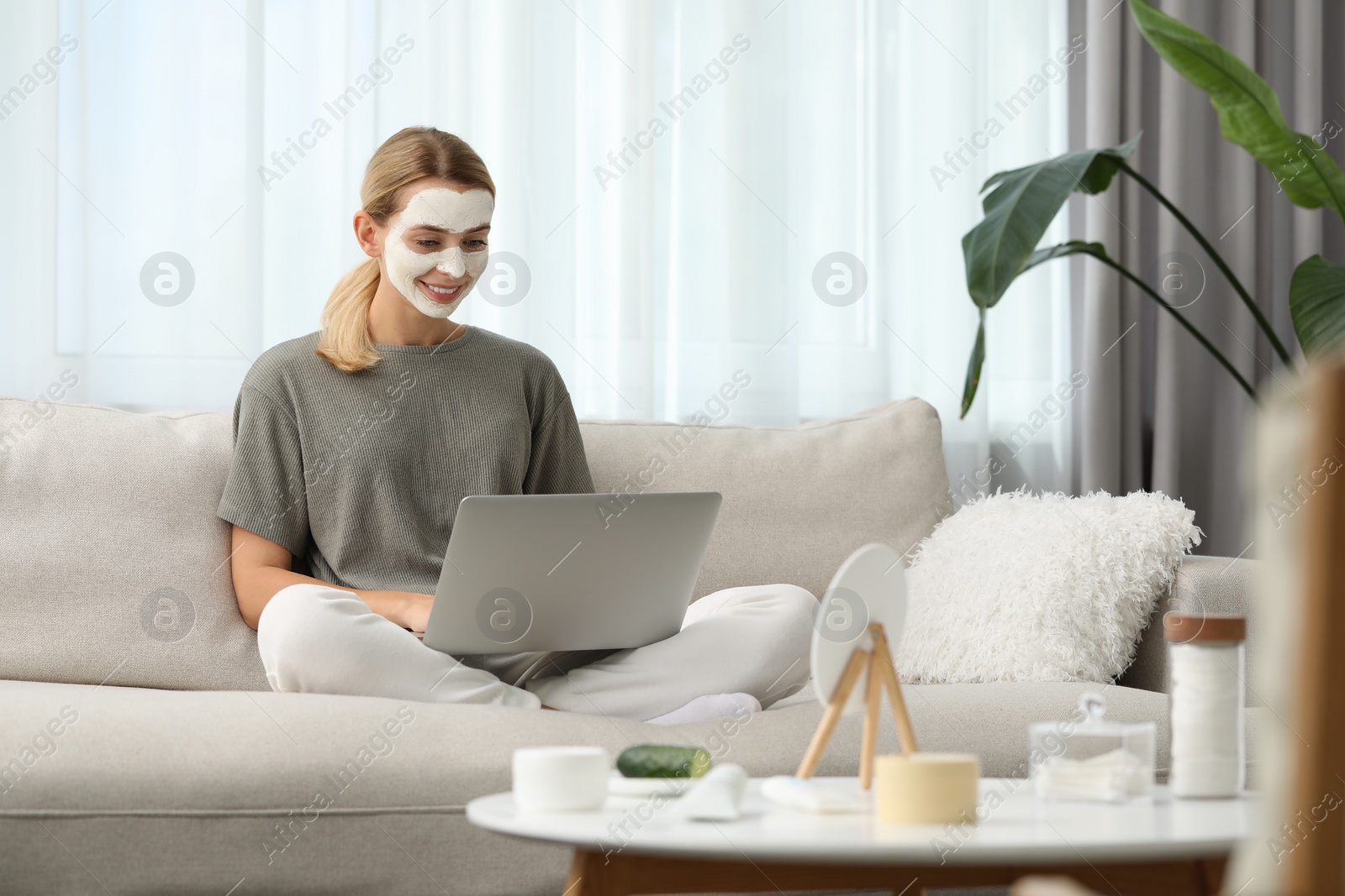 Photo of Young woman with face mask using laptop on sofa at home. Spa treatments