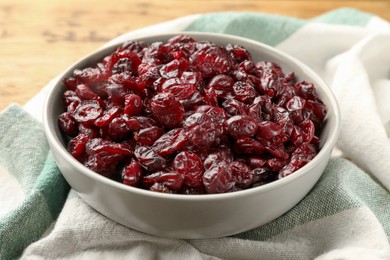 Photo of Tasty dried cranberries in bowl on wooden table, closeup