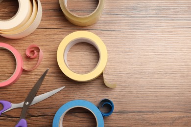 Photo of Rolls of adhesive tape and scissors on wooden background, flat lay. Space for text