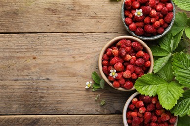 Photo of Fresh wild strawberries in bowls and leaves on wooden table, flat lay. Space for text