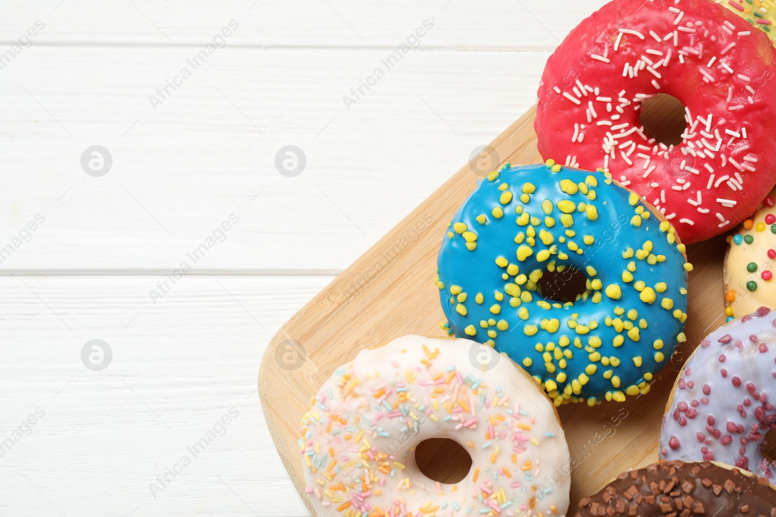 Photo of Yummy donuts with sprinkles on white wooden background, top view. Space for text