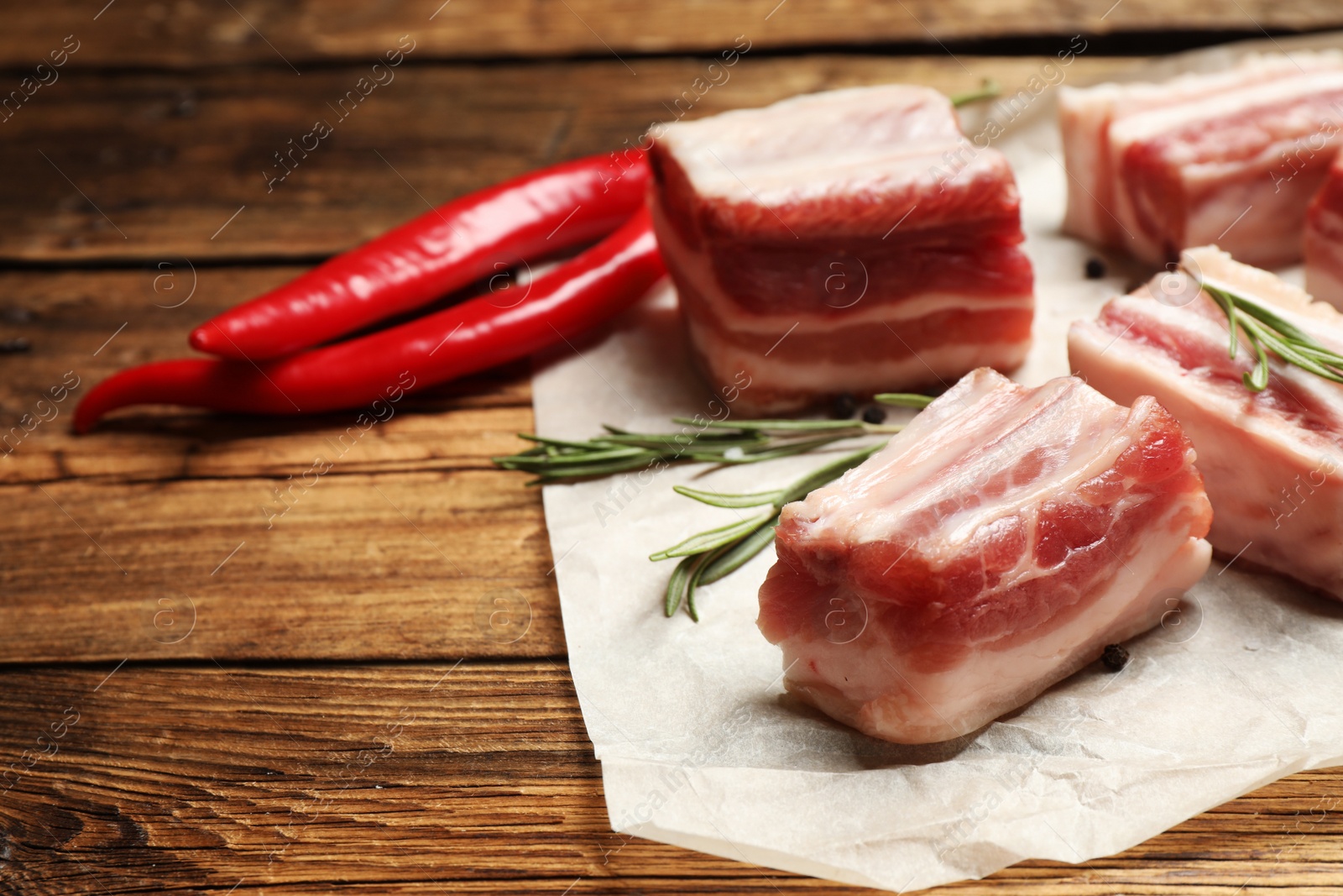 Photo of Raw ribs with rosemary on wooden table, closeup. Space for text