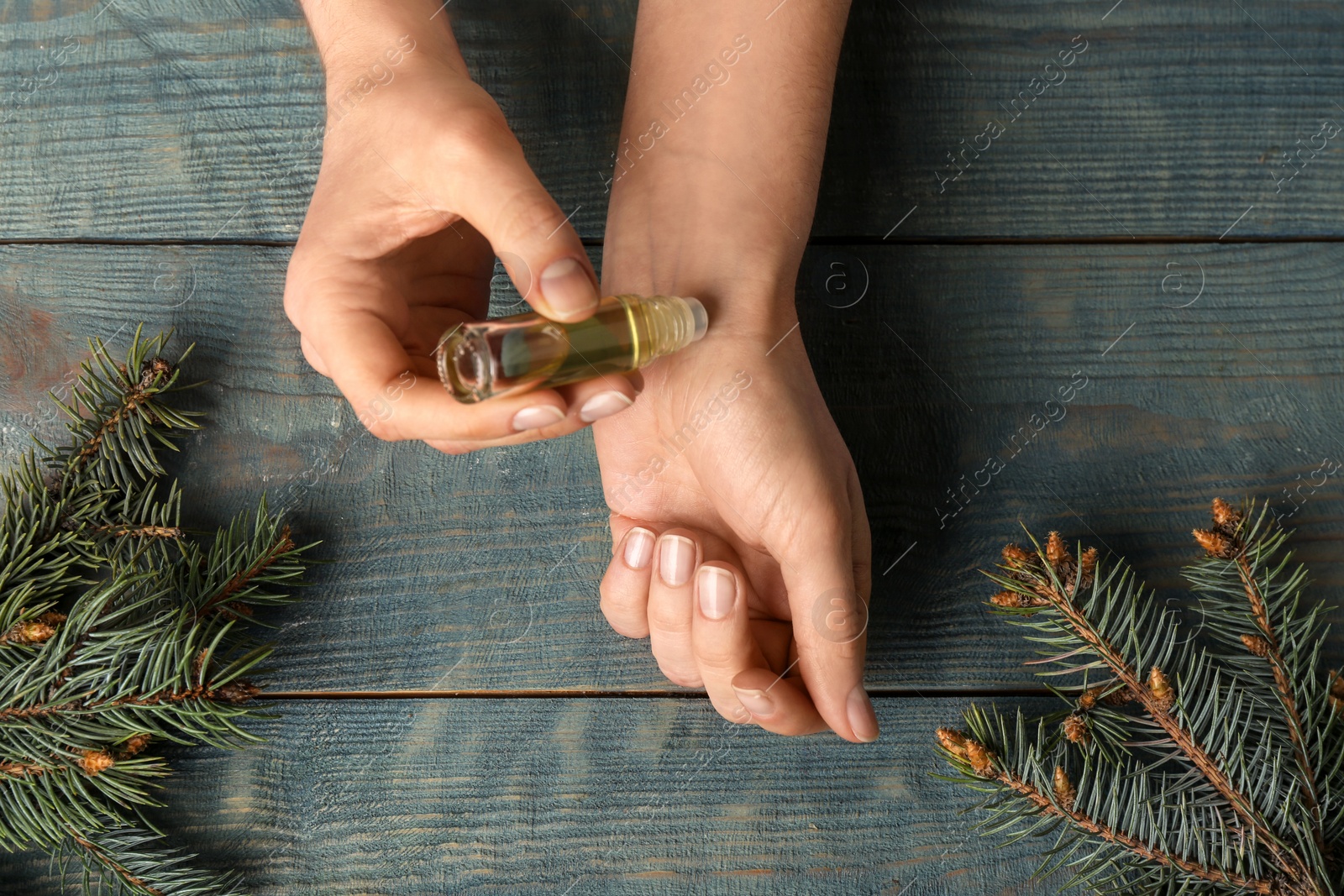Photo of Woman applying conifer essential oil on wrist over blue wooden table, closeup