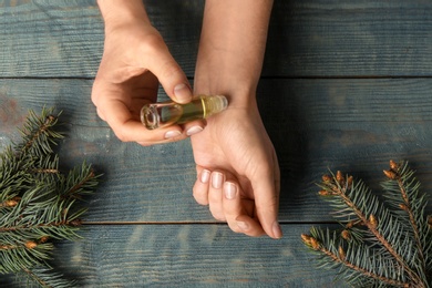 Photo of Woman applying conifer essential oil on wrist over blue wooden table, closeup