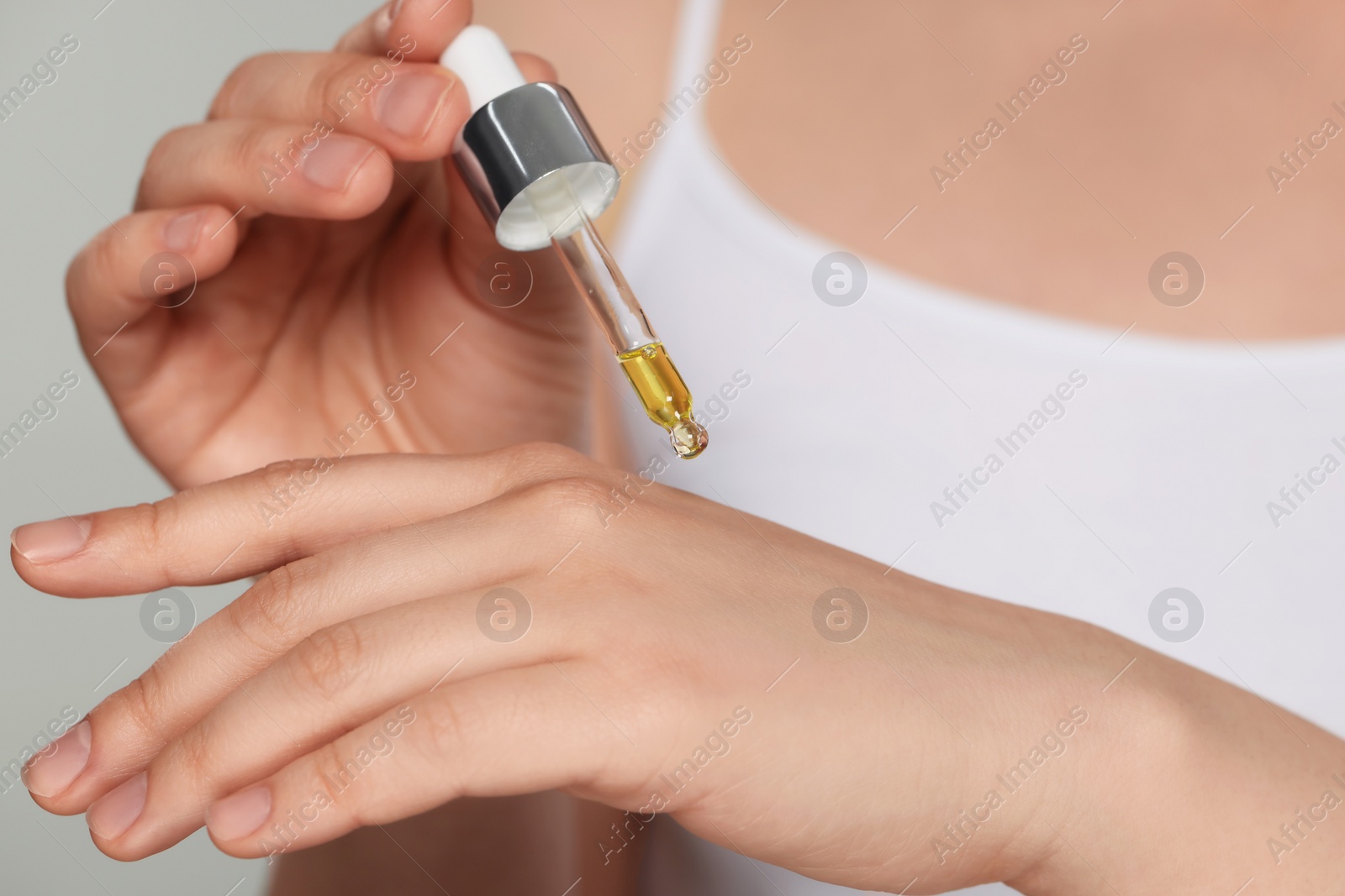 Photo of Woman applying essential oil onto hand on grey background, closeup