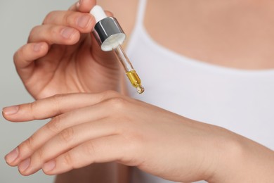 Photo of Woman applying essential oil onto hand on grey background, closeup