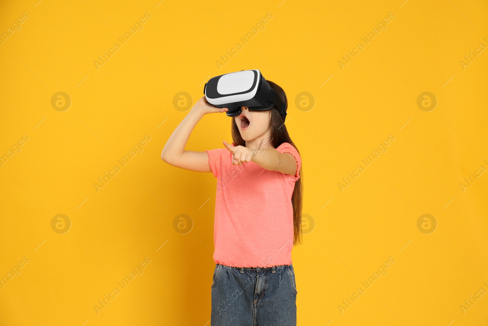 Photo of Emotional little girl using virtual reality headset on yellow background