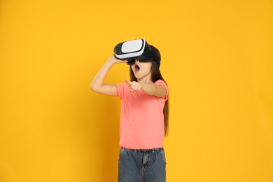 Photo of Emotional little girl using virtual reality headset on yellow background