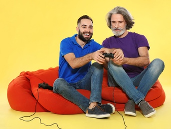 Mature man and guy playing video games with controllers on color background