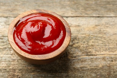 Photo of Tasty ketchup in bowl on wooden table, space for text. Tomato sauce