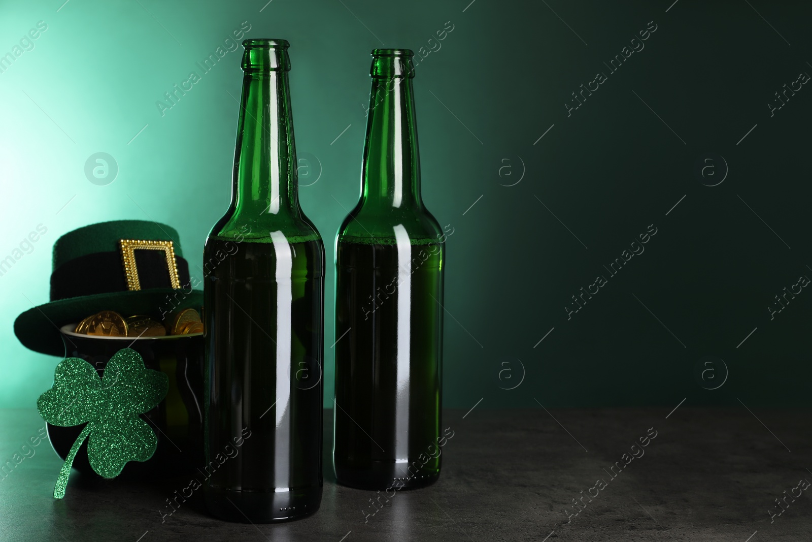 Photo of St. Patrick's day celebration. Beer in green bottles, leprechaun hat, pot of gold and decorative clover leaf on grey table. Space for text