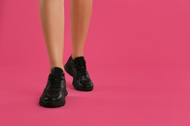 Woman wearing sneakers on pink background, closeup. Space for text