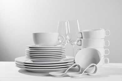 Photo of Set of clean dishware and glasses on white wooden table against light background