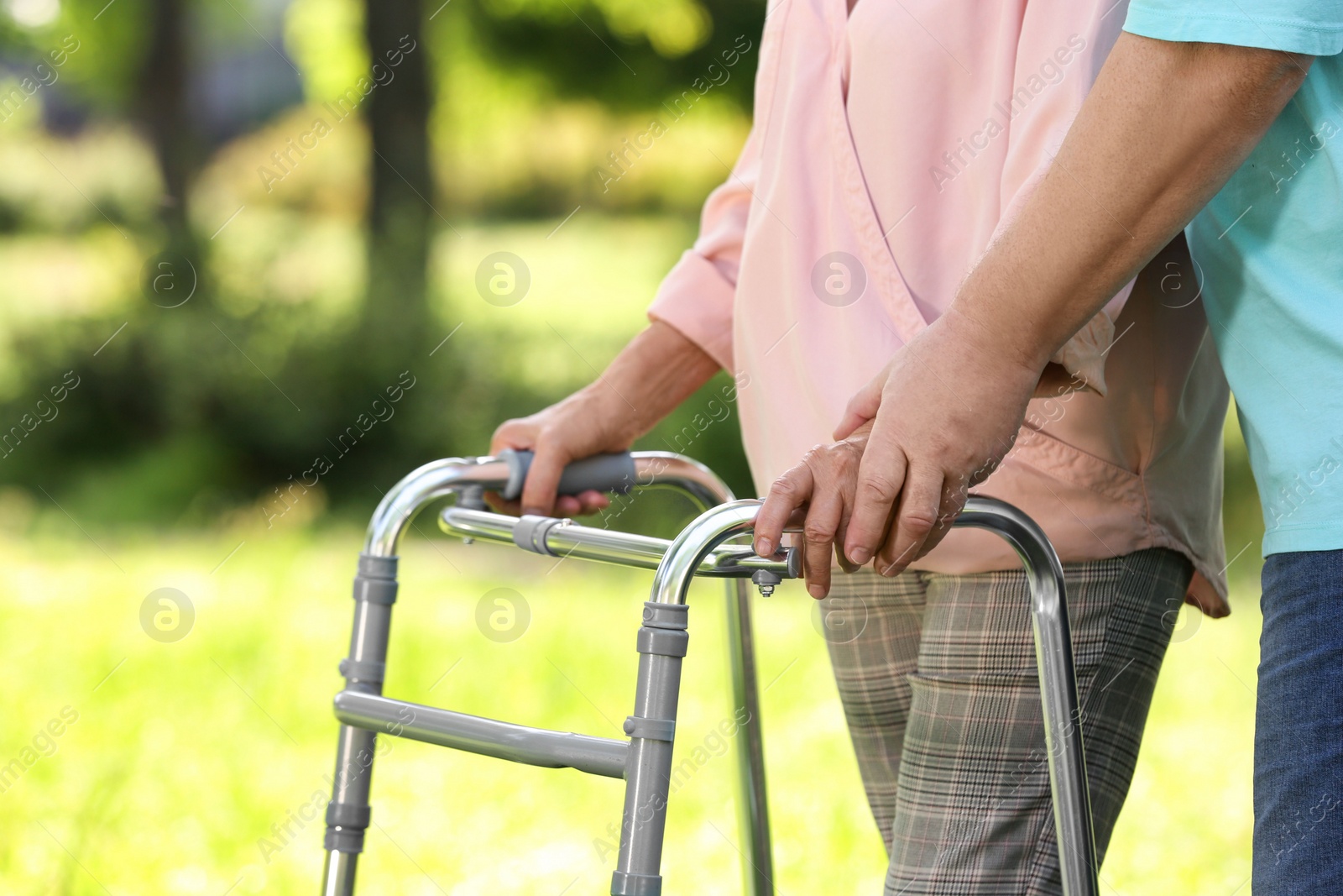 Photo of Elderly man helping his wife with walking frame outdoors, closeup