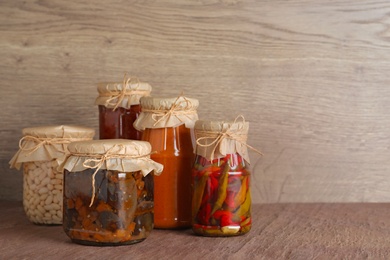 Photo of Jars of tasty pickled vegetables on brown table. Space for text