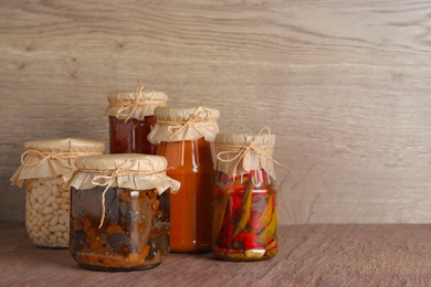 Jars of tasty pickled vegetables on brown table. Space for text