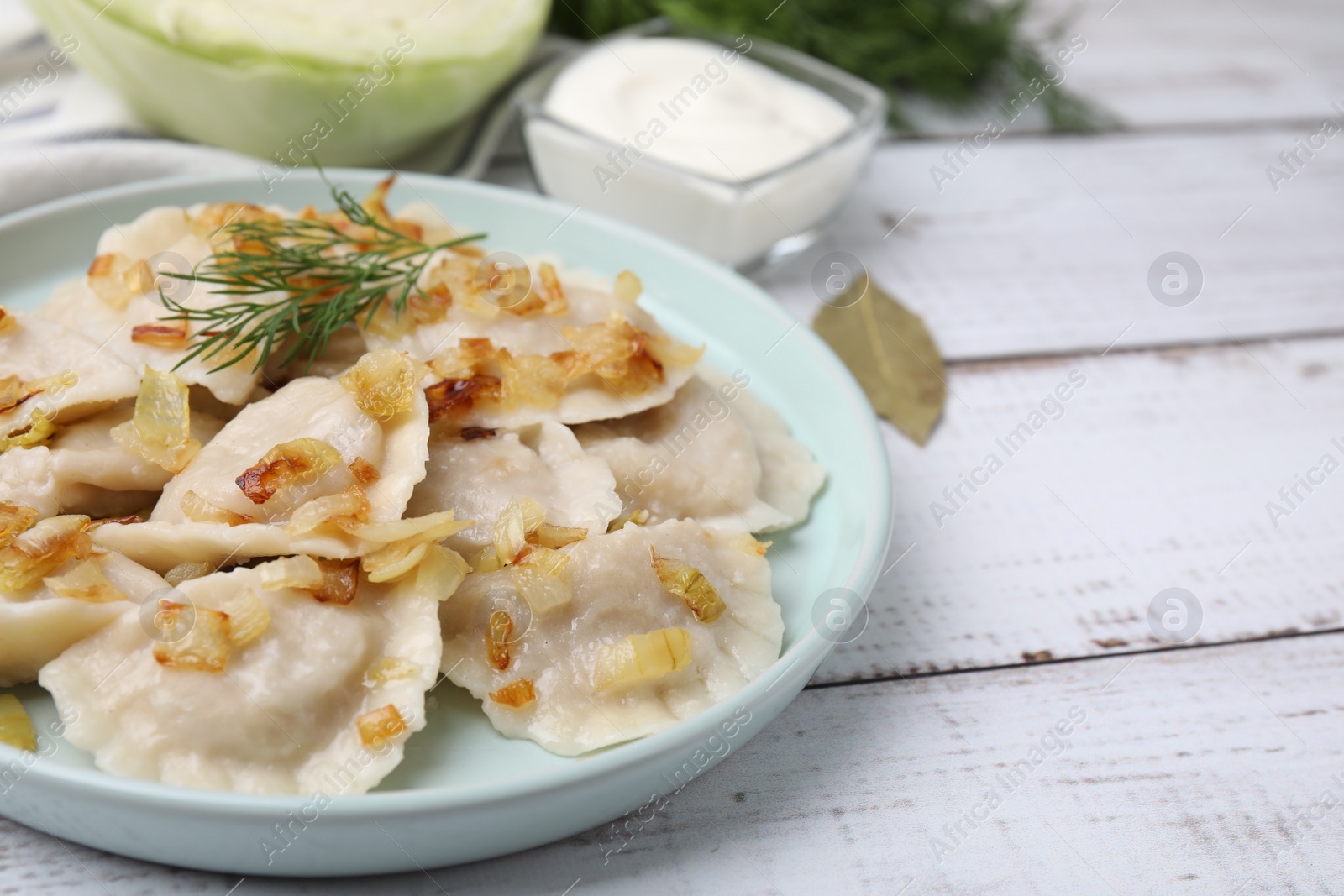 Photo of Cooked dumplings (varenyky) with tasty filling, fried onions and dill on wooden table, closeup