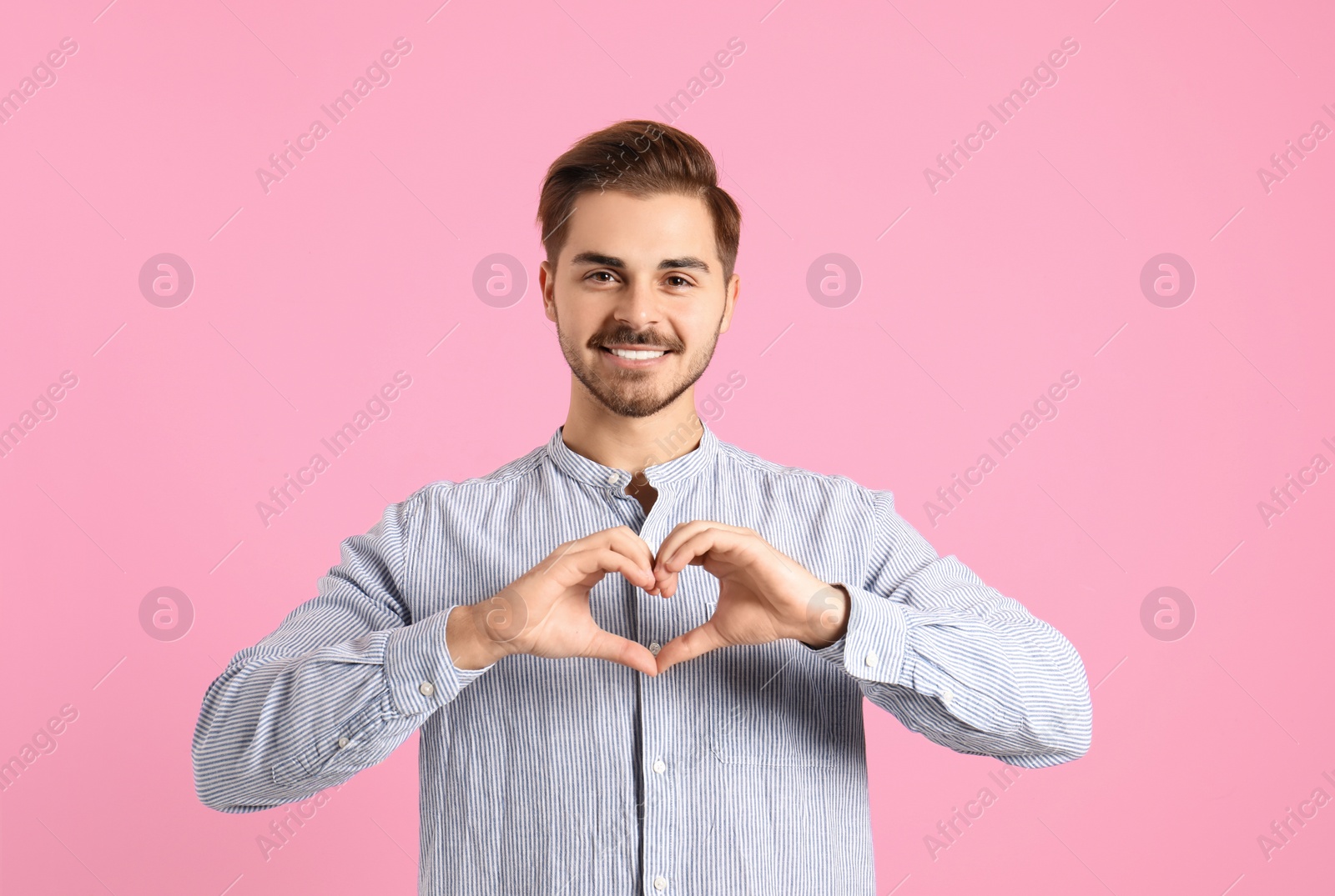 Photo of Portrait of young man making heart with his hands on color background