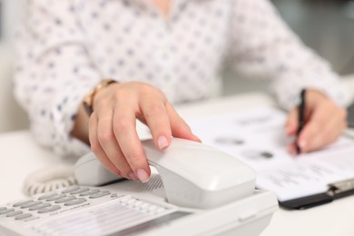 Photo of Secretary taking telephone handset at table in office, closeup